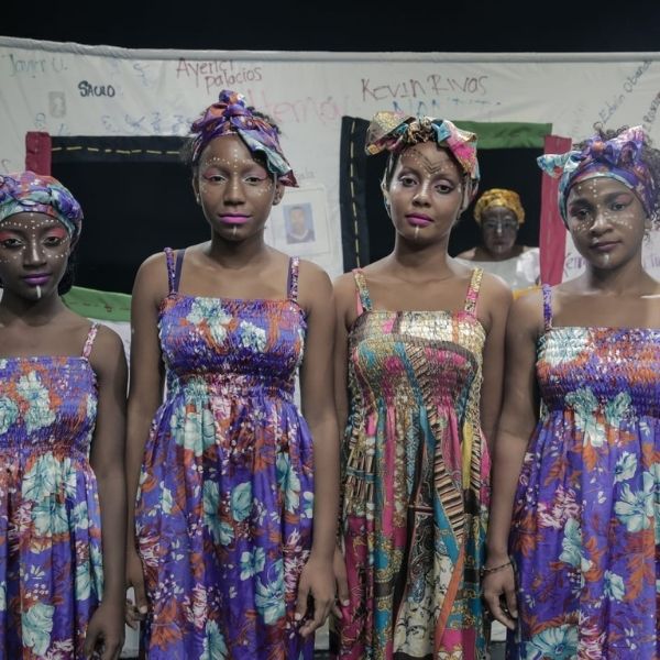 Hay cuatro artistas afrocolombianas, cada una de ellas tiene la cara pintada, tienen vestidos morados algunos con flores otros c