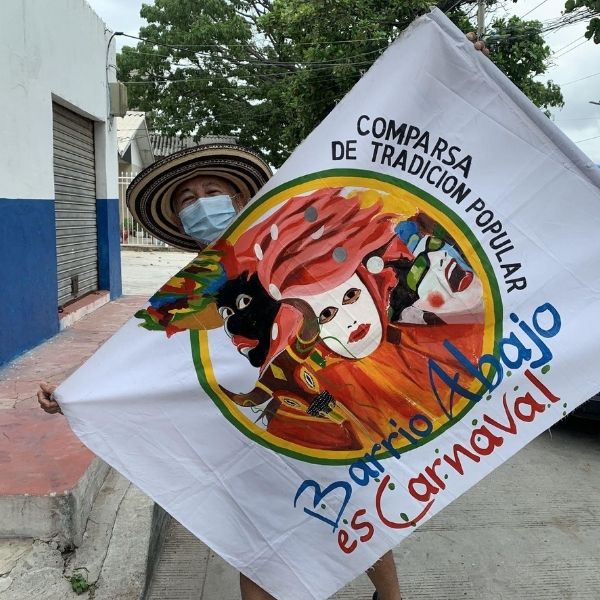 Hombre sostiene bandera con el mensaje Comparsa de Tradición Popular, Barrio Abajo es Carnaval